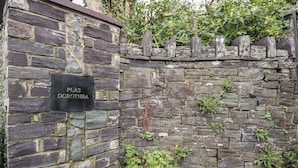 A stone wall with a sign reading "PLAS DOROTHEA" and a wooden barrel planter with plants. - Plas Dorothea (Caernarfon)
