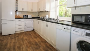 A kitchen with white cabinets, a washing machine, a dishwasher, and a microwave. - Plas Dorothea (Caernarfon)