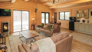 L’intérieur d’une cabane en rondins, avec une cheminée, des canapés en cuir, une table à manger et un coin cuisine.