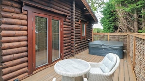 Une cabane en rondins dotée d’une terrasse avec des meubles en osier et un jacuzzi.