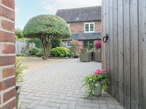 A brick house with a paved patio, a round hedge, and a wooden fence. - The Creamery (Burton on Trent)