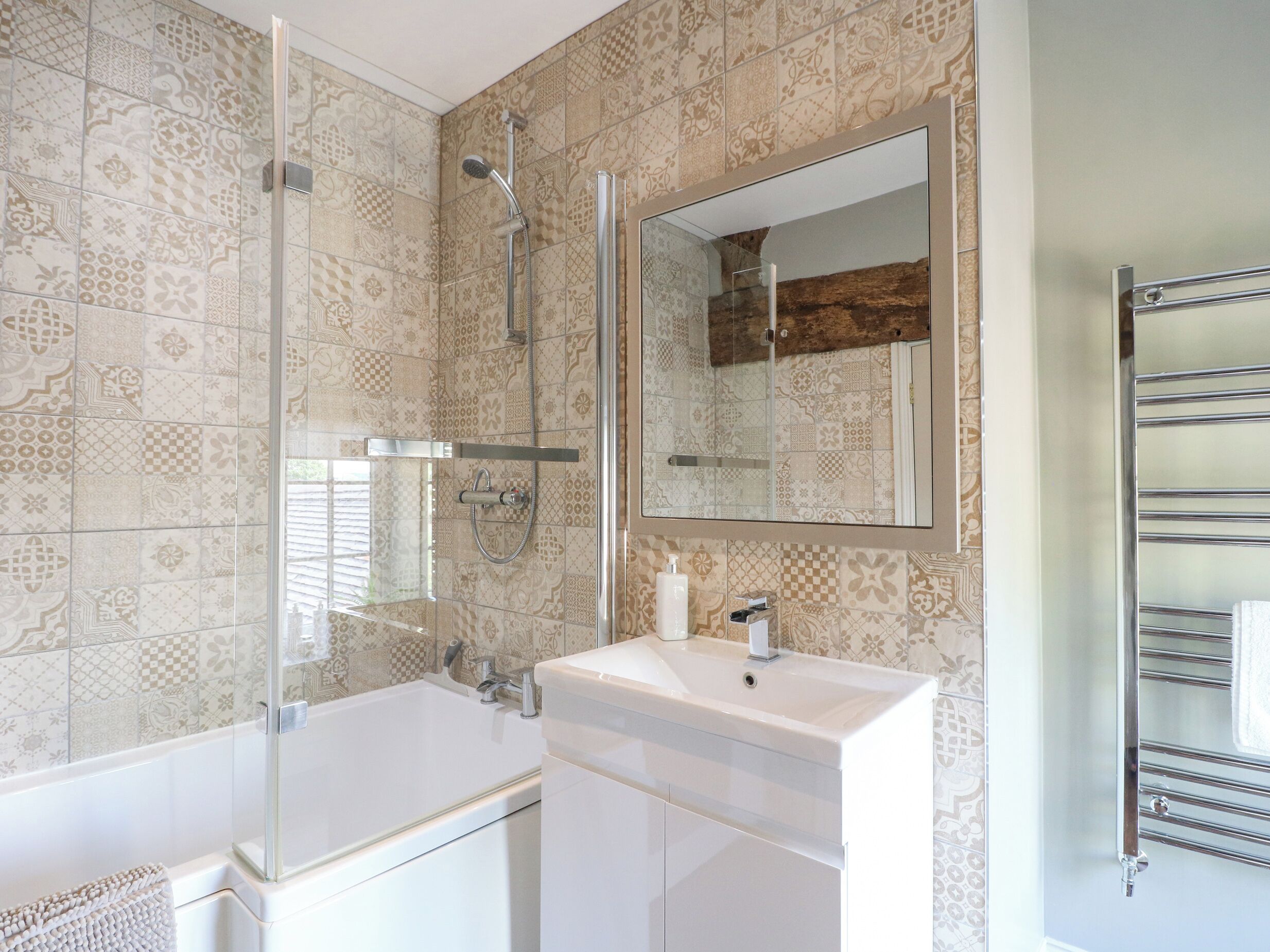 A modern bathroom with patterned tiles, a glass-enclosed shower, a white sink, and a towel rack.
