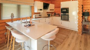Een moderne keuken met houten wanden, witte kasten, een centraal eiland met barstoelen en een inbouwoven.
