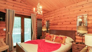 Een slaapkamer in een houten blokhut met een groot bed, twee nachtkastjes, een bedbank en een raam met gordijnen.