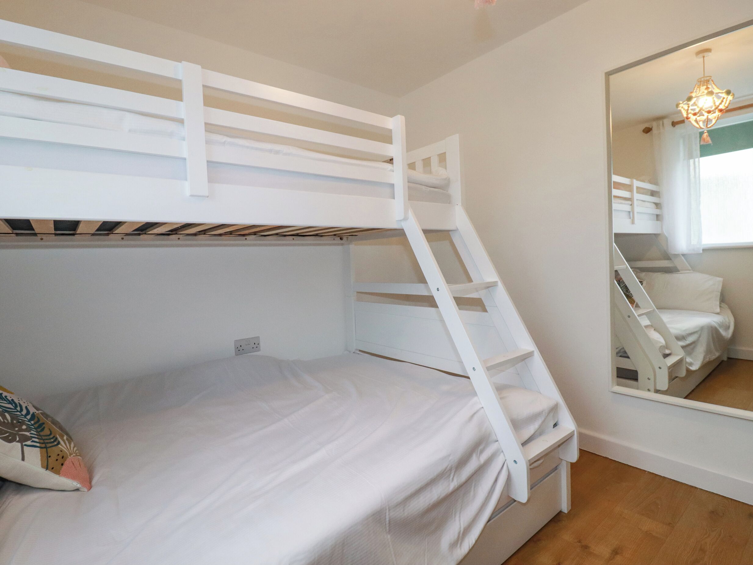 A bunk bed with a ladder, a bedside table, and a mirror reflecting the room.