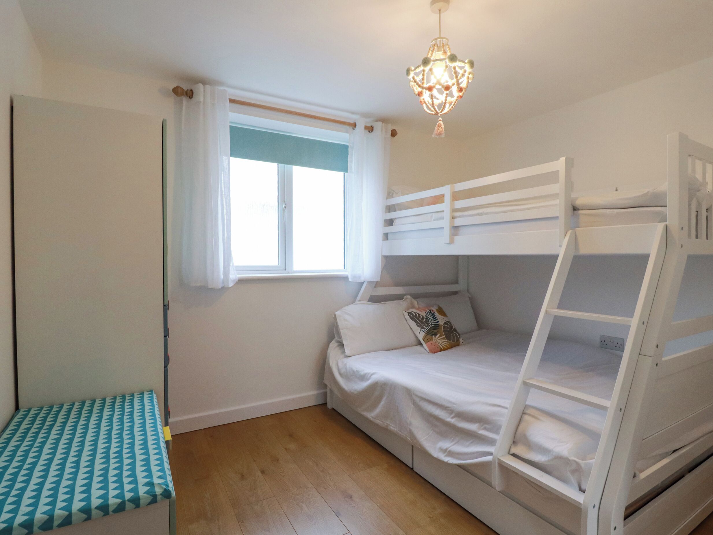 Una camera da letto con una cuccetta, un comodino, una finestra con tende e un lampadario.