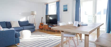 A modern living room with a blue sofa, a wooden dining table, and a TV.