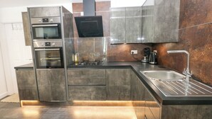 A modern kitchen with stainless steel appliances, a built-in oven, a range hood, and a sink. - Apartment 4 (Tenby)