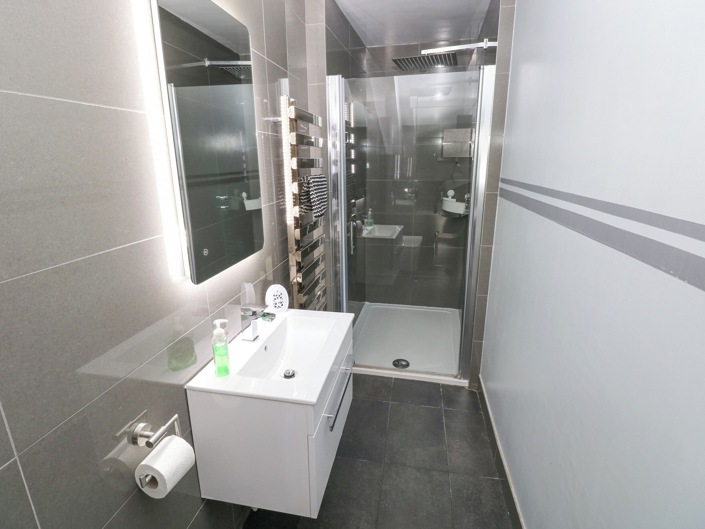 Moderni kylpyhuone, jossa on lasinen suihkuseinä, valkoinen pesuallas ja sen yläpuolella peili sekä wc-istuin.