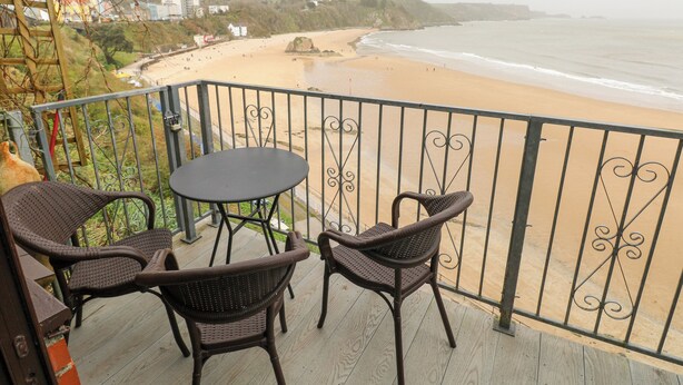 A balcony with wicker chairs and a table overlooking a beach. - Apartment 4 (Tenby)