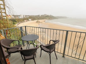 A balcony with wicker chairs and a table overlooking a beach. - Apartment 4 (Tenby)