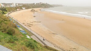A coastal beach with a sandy shore, a rocky outcrop, and a promenade with boats. - Apartment 4 (Tenby)