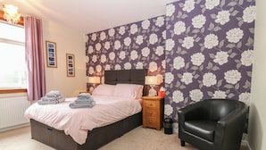 A bedroom with a bed, a nightstand, a chair, and a floral wallpaper. - Thain House (Banff)