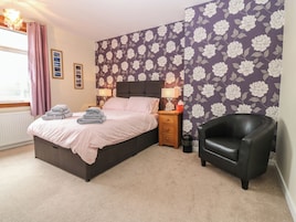 A bedroom with a bed, a nightstand, a chair, and a floral wallpaper.