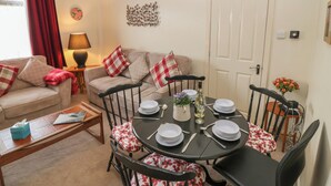 A dining area with a round table set for four, surrounded by four chairs with floral cushions. A sofa with red and white checkered cushions is positioned against the wall, and a lamp is on a side table. - Thain House (Banff)