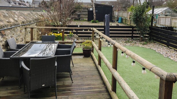 An outdoor deck with wicker furniture and a view of the surrounding area including a garden and buildings. - Thain House (Banff)