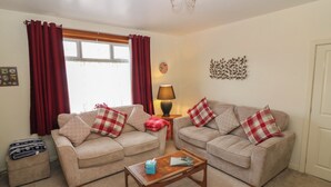 A living room with two beige sofas, a wooden coffee table, and a lamp. - Thain House (Banff)