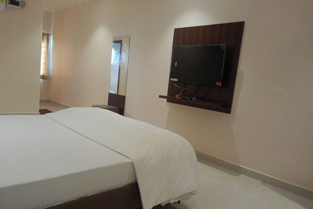 Une chambre d’hôtel avec un grand lit, un téléviseur à écran plat fixé au mur et un miroir au-dessus du lit.