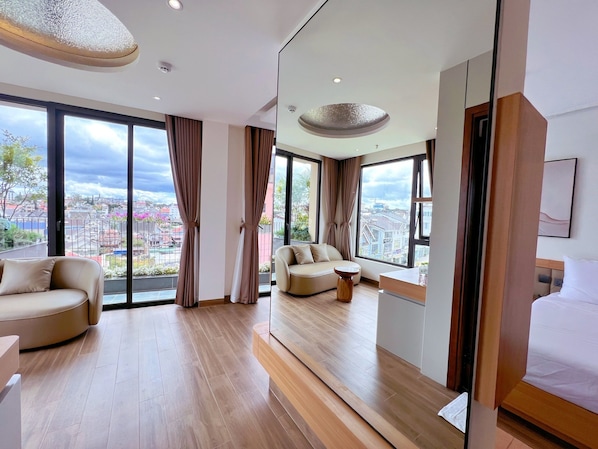 A modern hotel room with a large window, a sofa, a small table, and a bed.
