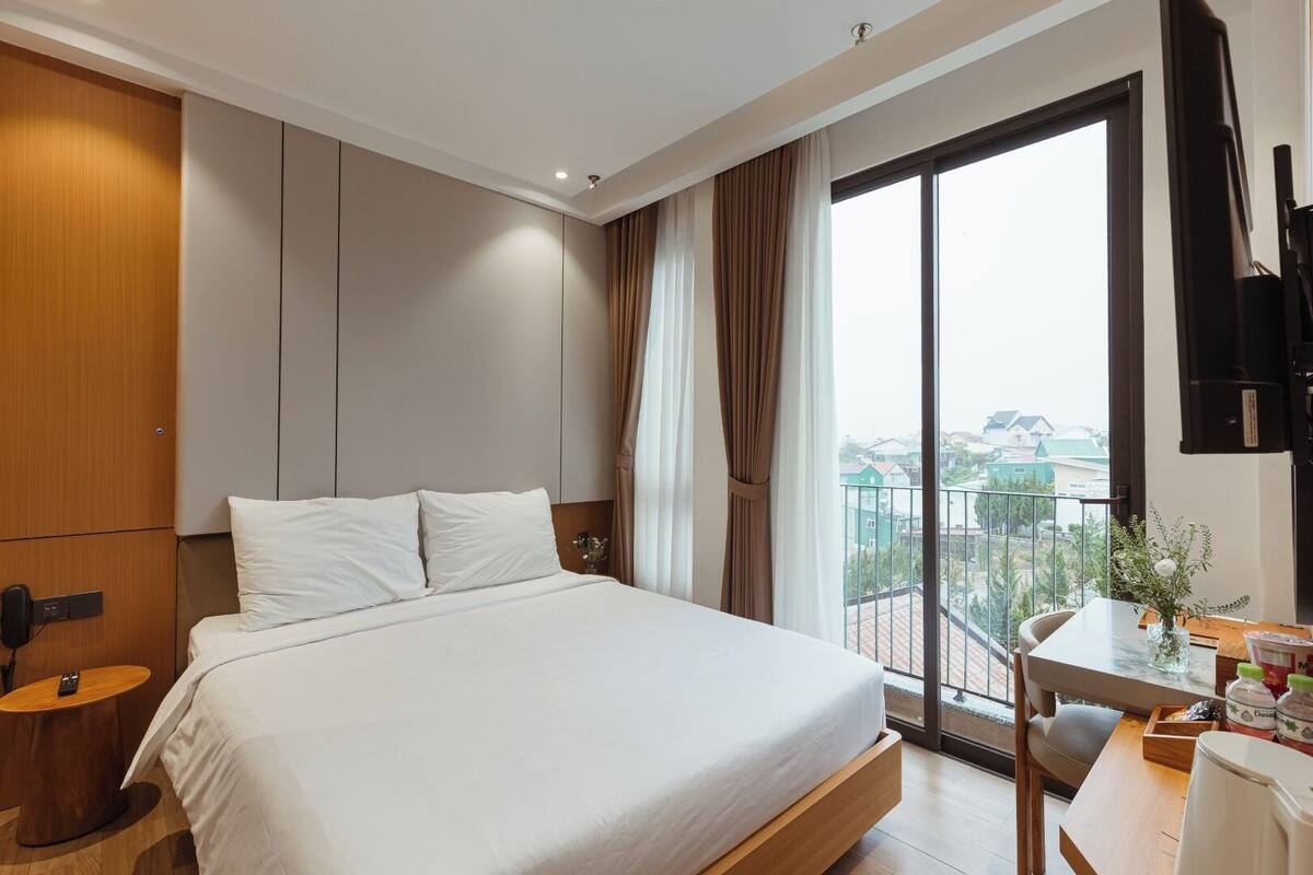 Habitación de hotel con una cama grande, un escritorio con silla, televisor y balcón con vistas.