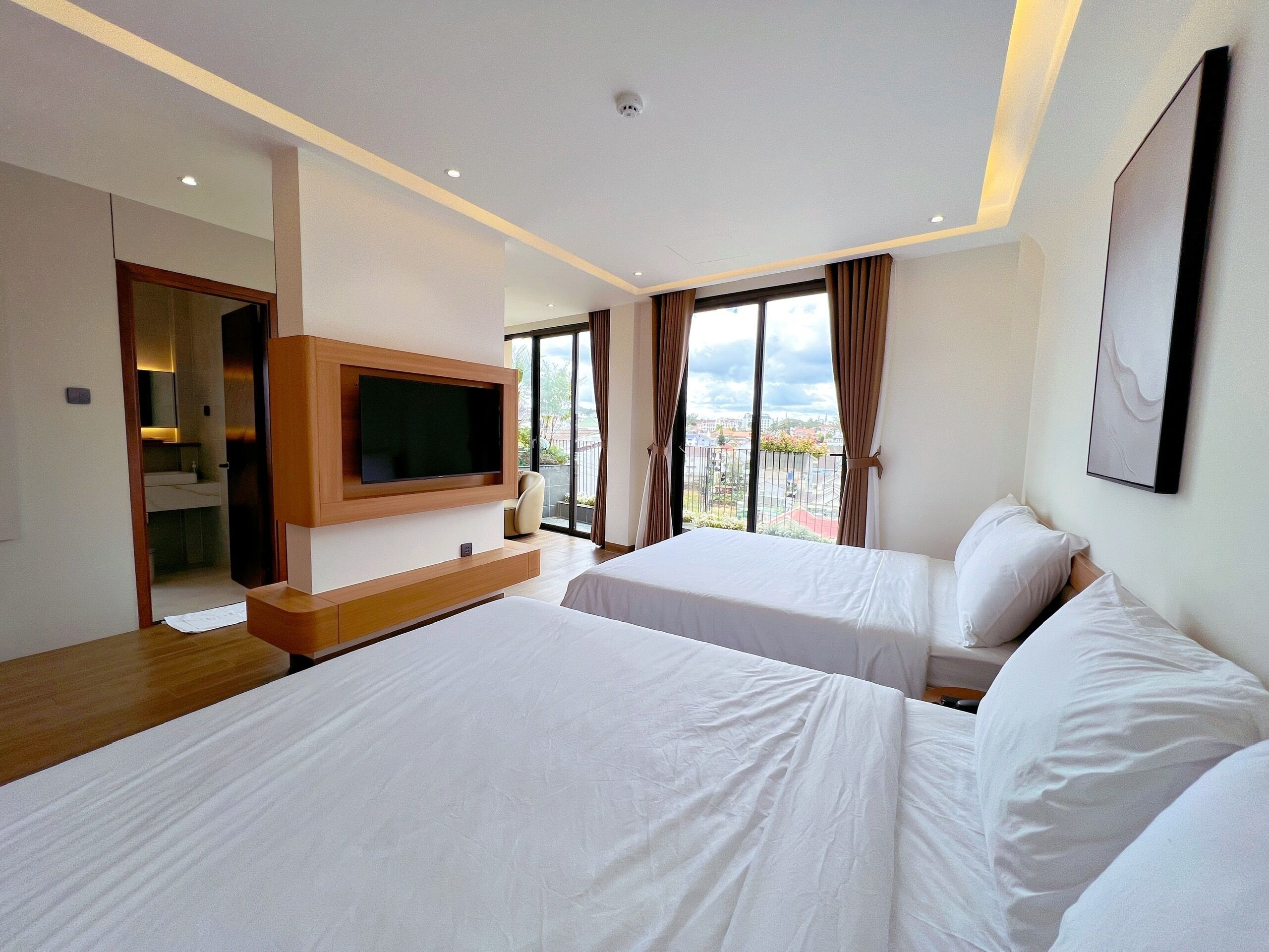 A hotel room with two beds, a TV mounted on the wall, and a balcony with a view.