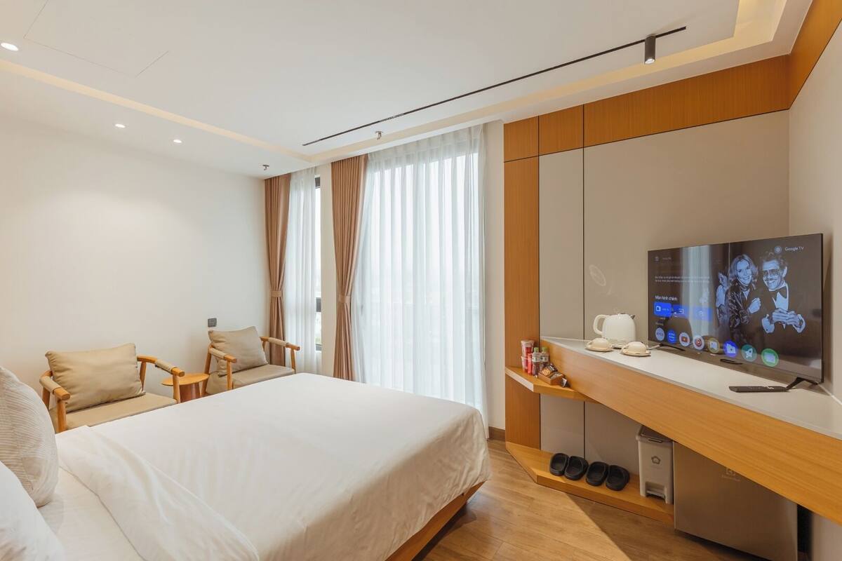 Una habitación de hotel moderna con cama, televisión, escritorio con cafetera y zapatero.