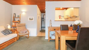 A cozy living room with a sofa, a wooden dining table with chairs, a bookshelf, and a kitchen area with a stove and cabinets. - Glaslyn Retreat (Porthmadog)