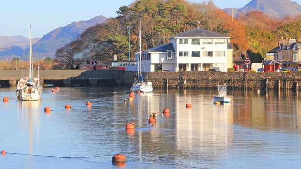 A harbor with boats, a stone wall, and a building with a white facade. - Glaslyn Retreat (Porthmadog)