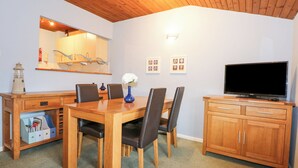 A dining area with a wooden table, chairs, a vase with flowers, a television, and a cabinet. - Glaslyn Retreat (Porthmadog)