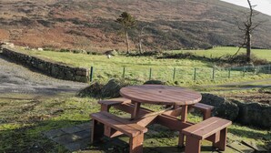 A picnic table with benches in a rural setting with a stone wall and a grassy field. - Dan White's Cottage (Newry)