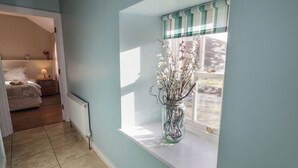 A room with a window sill, a radiator, a bed, and a vase with branches. - Dan White's Cottage (Newry)