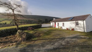 A white house with a red door, a stone wall, and a picnic table in a rural setting. - Dan White's Cottage (Newry)