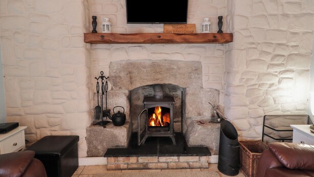 A stone wall with a fireplace, a mounted television, and a sign reading "Welcome to Dan White's Cottage." - Dan White's Cottage (Newry)