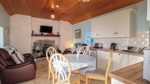 A cozy living room with a fireplace, a dining area with a table and chairs, and a kitchen with white cabinets and wooden countertops. - Dan White's Cottage (Newry)