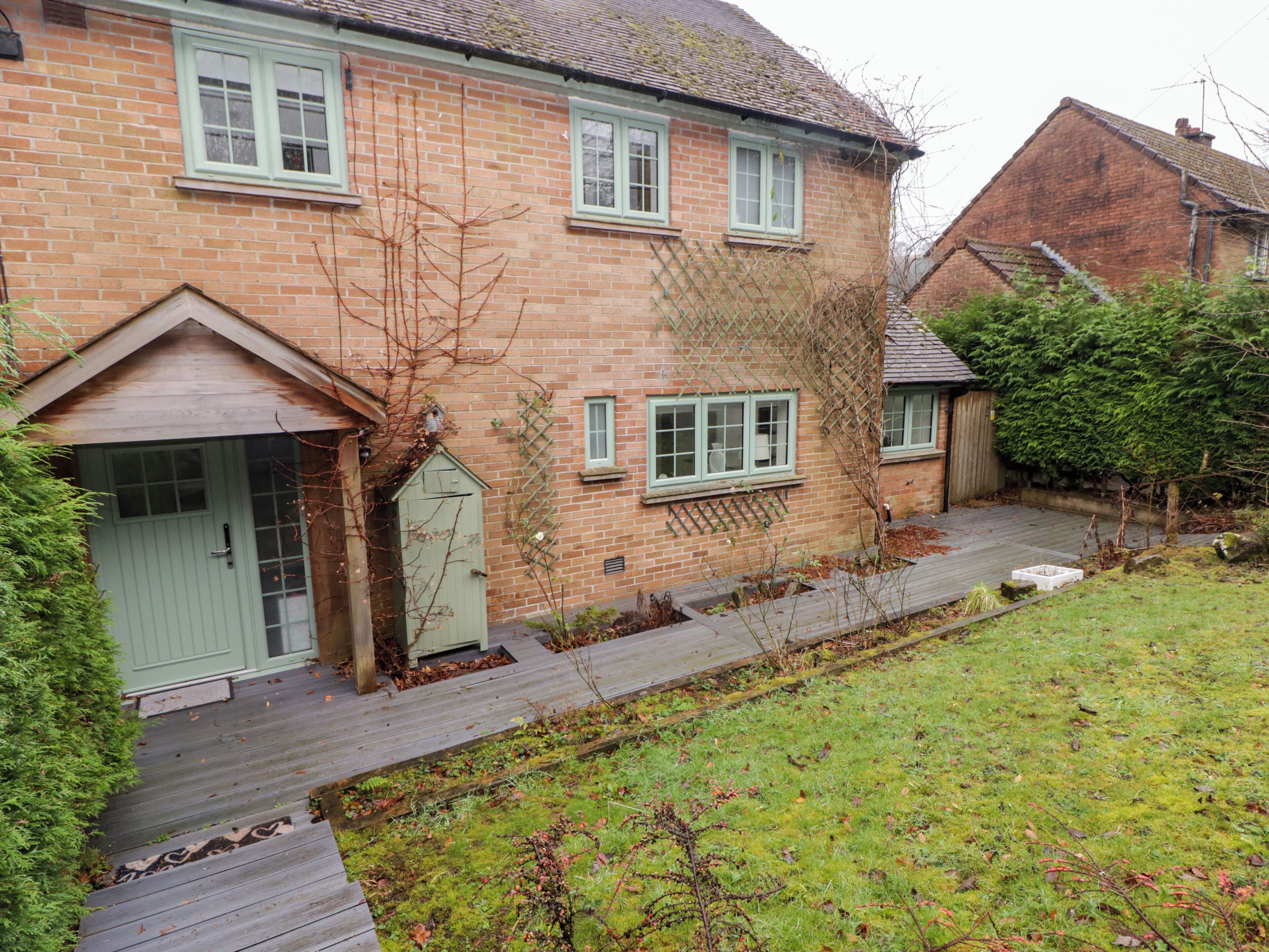 A two-story brick house with a green door, a small garden, and a wooden pathway leading to the front door.