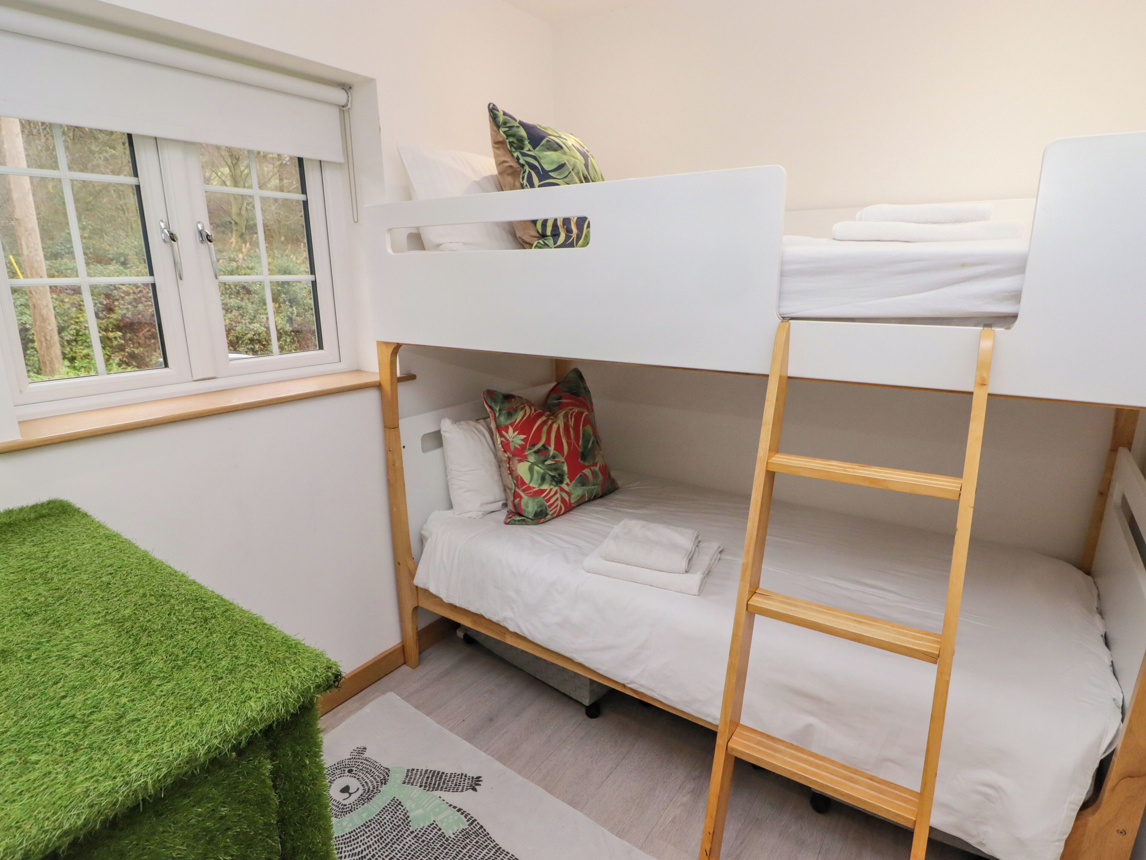 A bunk bed room with a window, a green rug, and a white bedspread.