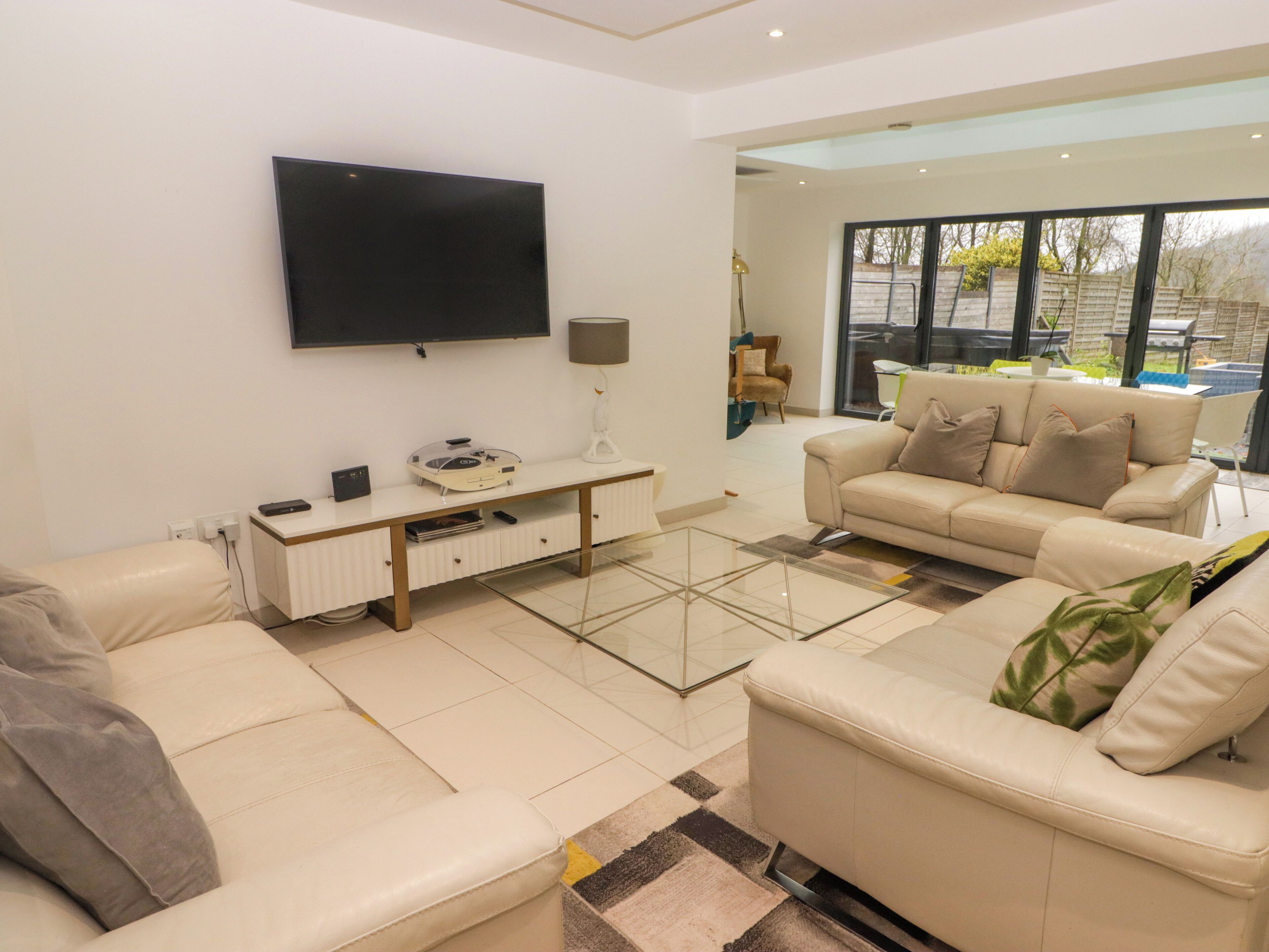 Una sala de estar moderna con un televisor de pantalla plana montado en la pared, un sofá blanco, un sofá beige y una mesa de centro de vidrio.