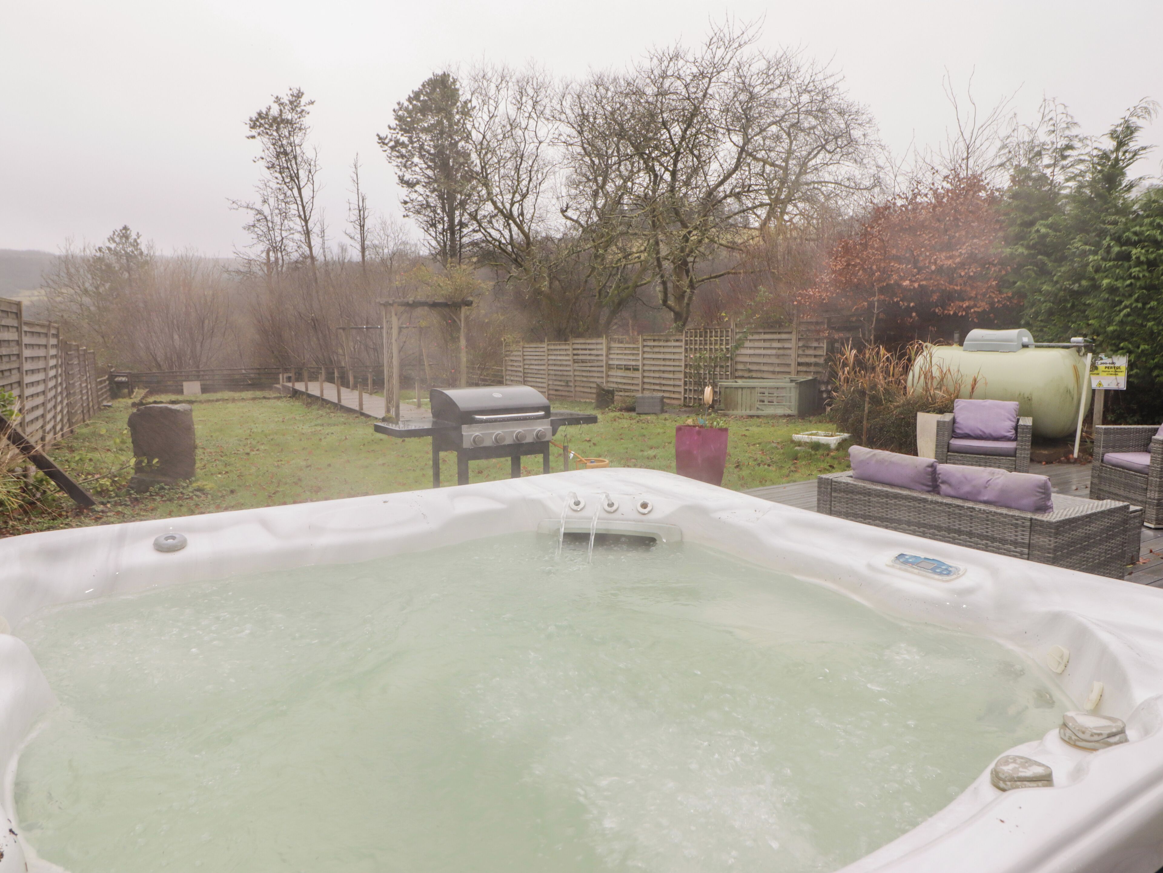 A hot tub in a backyard with a grill and outdoor furniture.