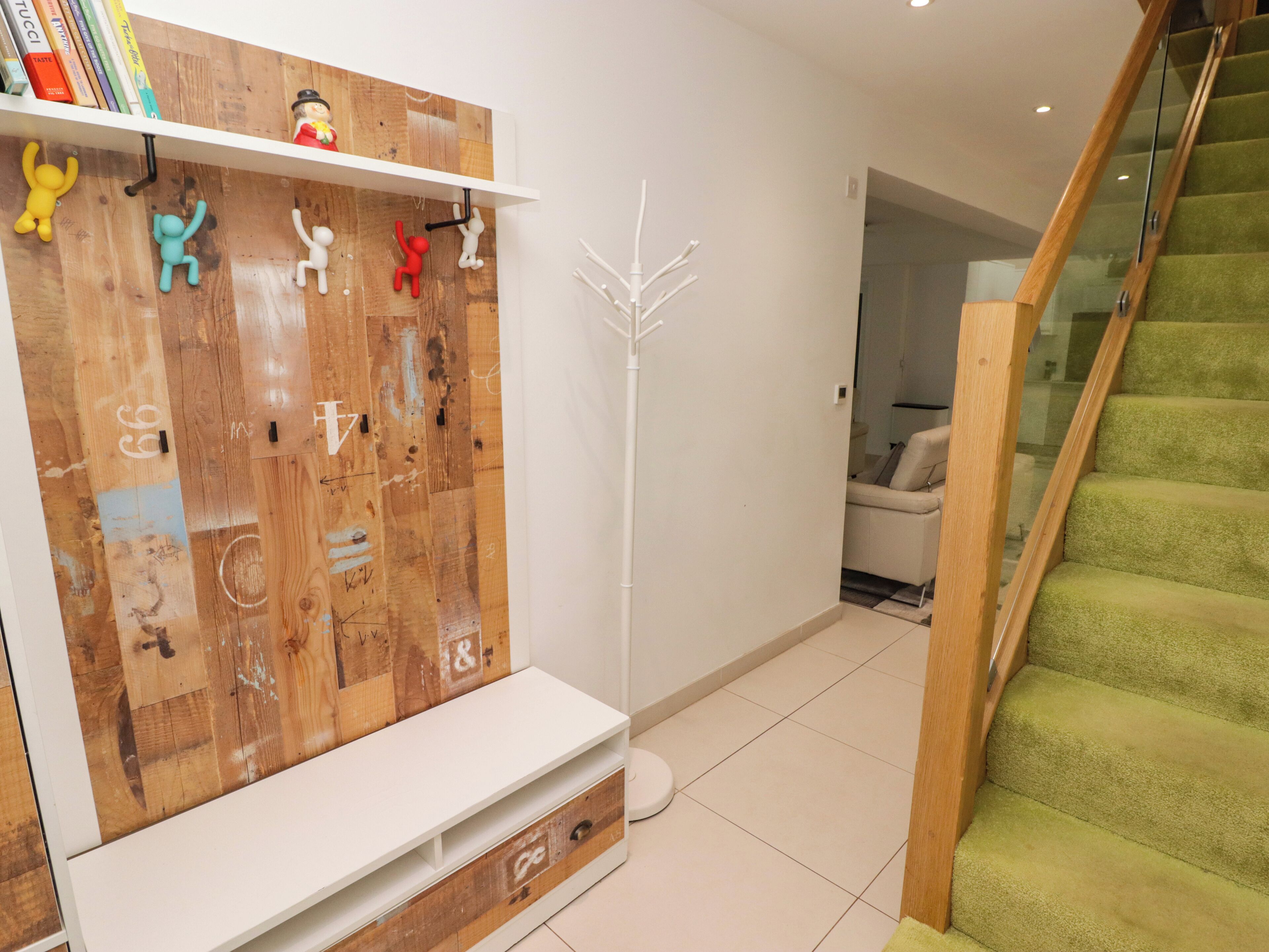 Un salon moderne avec un meuble mural en bois, un lampadaire blanc et un escalier recouvert d’une moquette verte.