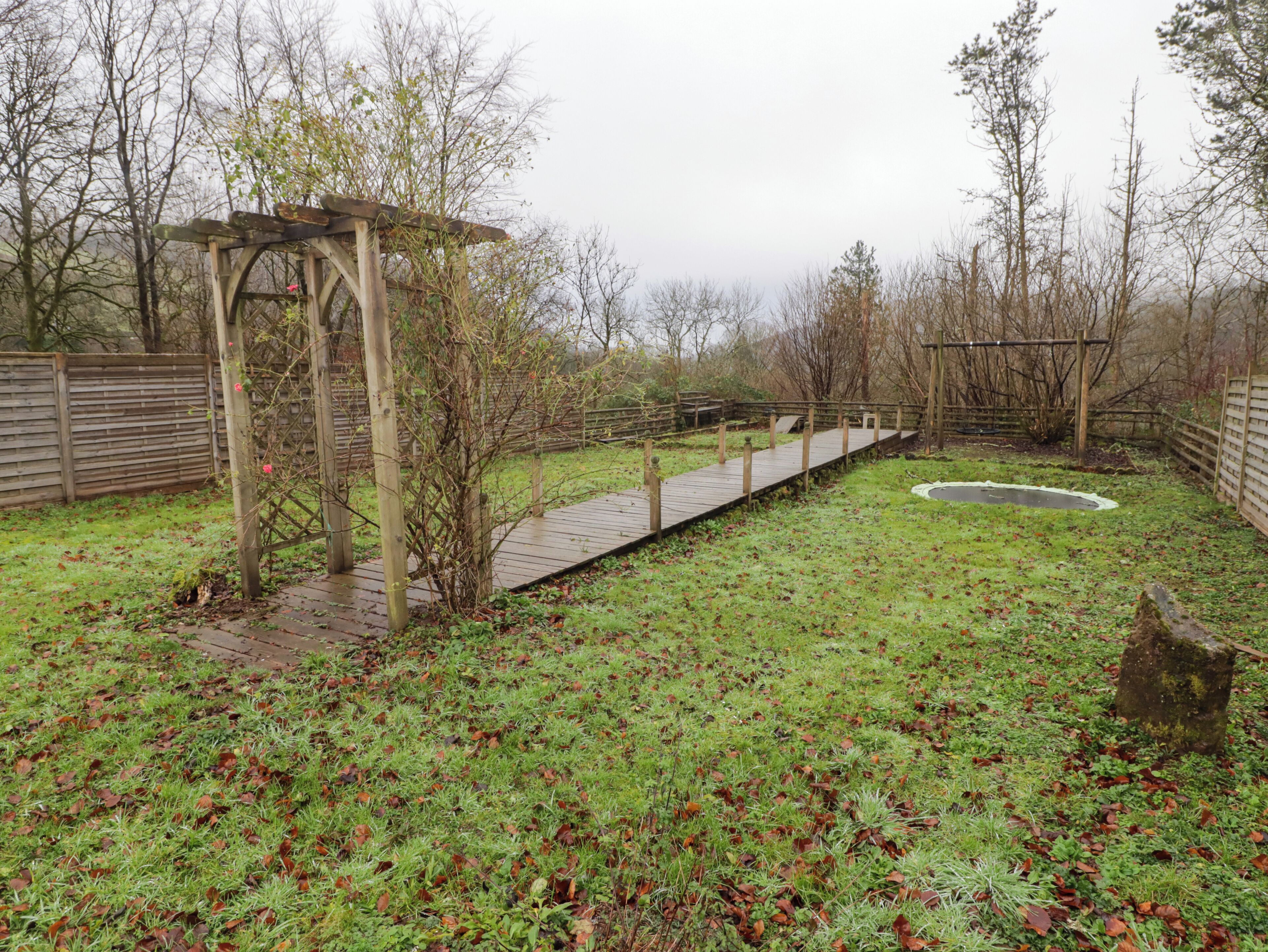 Eine Holzterrasse mit einer Pergola, umgeben von einer Rasenfläche mit verstreuten Blättern.
