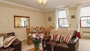 A living room with a brown leather sofa, a wooden coffee table, and a dining area with wooden chairs and a table. - The Old Assembly Rooms (Bishop Auckland)