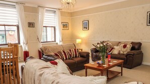 A cozy living room with a brown sofa, a wooden coffee table, and a dining area with a wooden table and chairs. - The Old Assembly Rooms (Bishop Auckland)