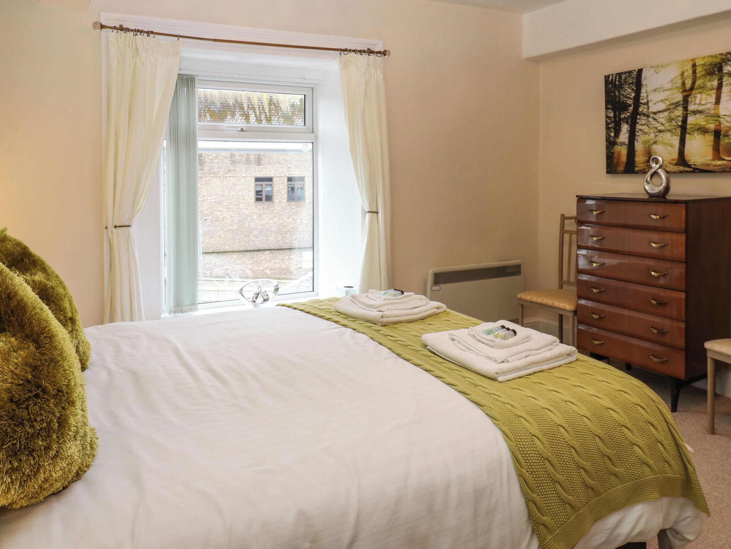 Una habitación de hotel con cama, cómoda, ventana con cortinas y un cuadro en la pared.