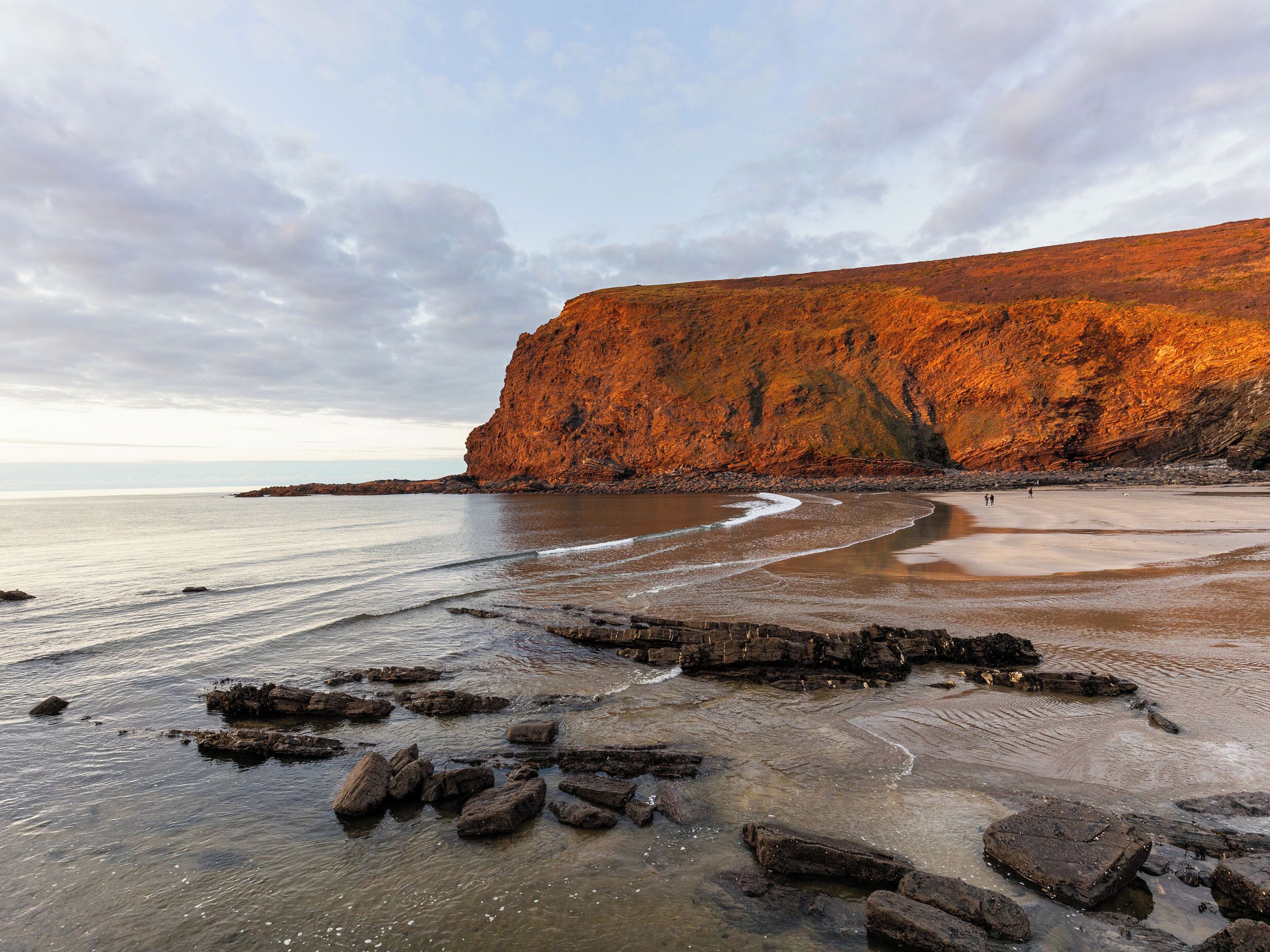 Eine Küstenlandschaft mit einer markanten Klippe, einem Sandstrand und verstreuten Felsen.