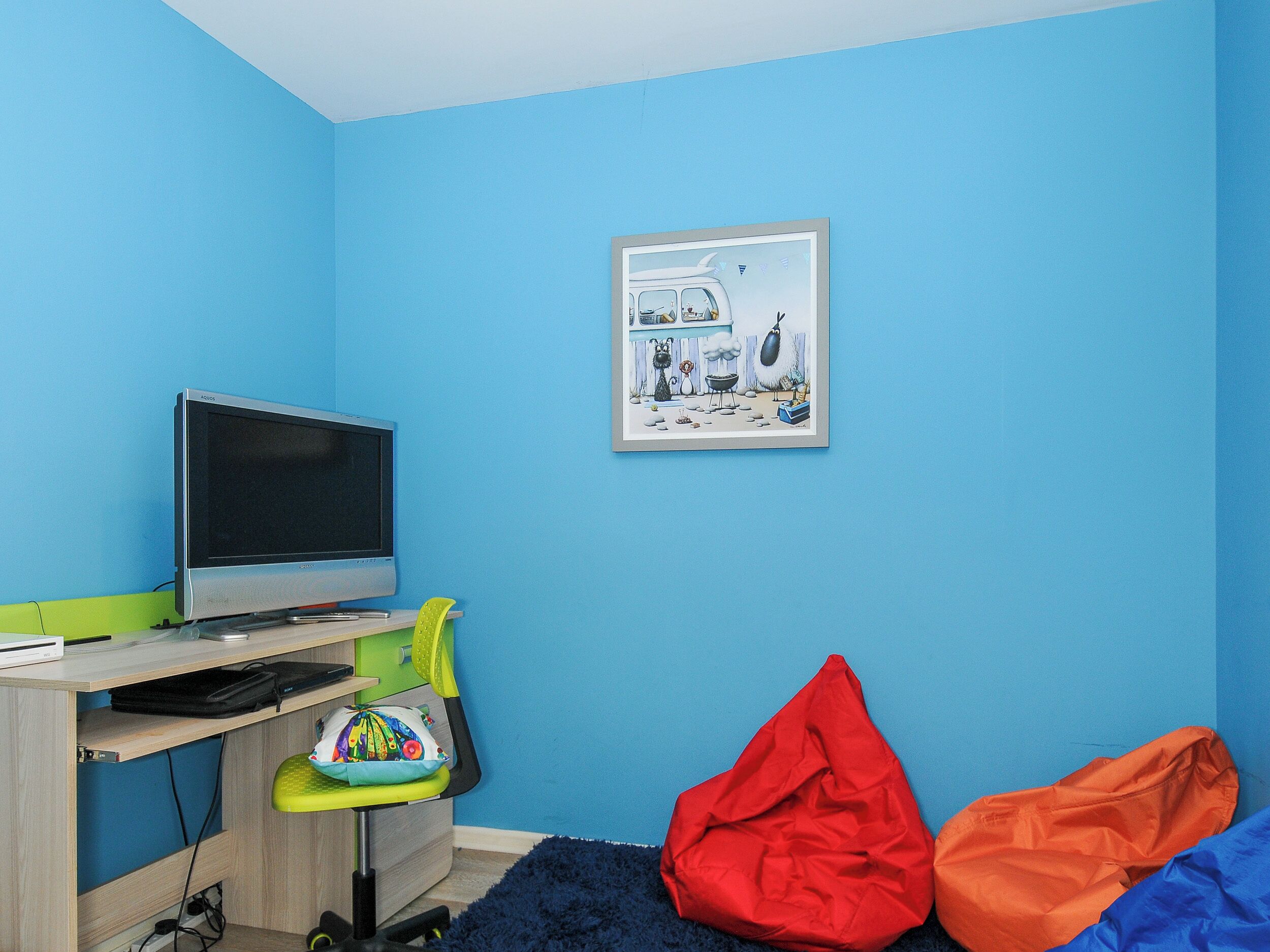 A room with a blue wall, a desk with a computer, a chair, and a colorful bean bag.