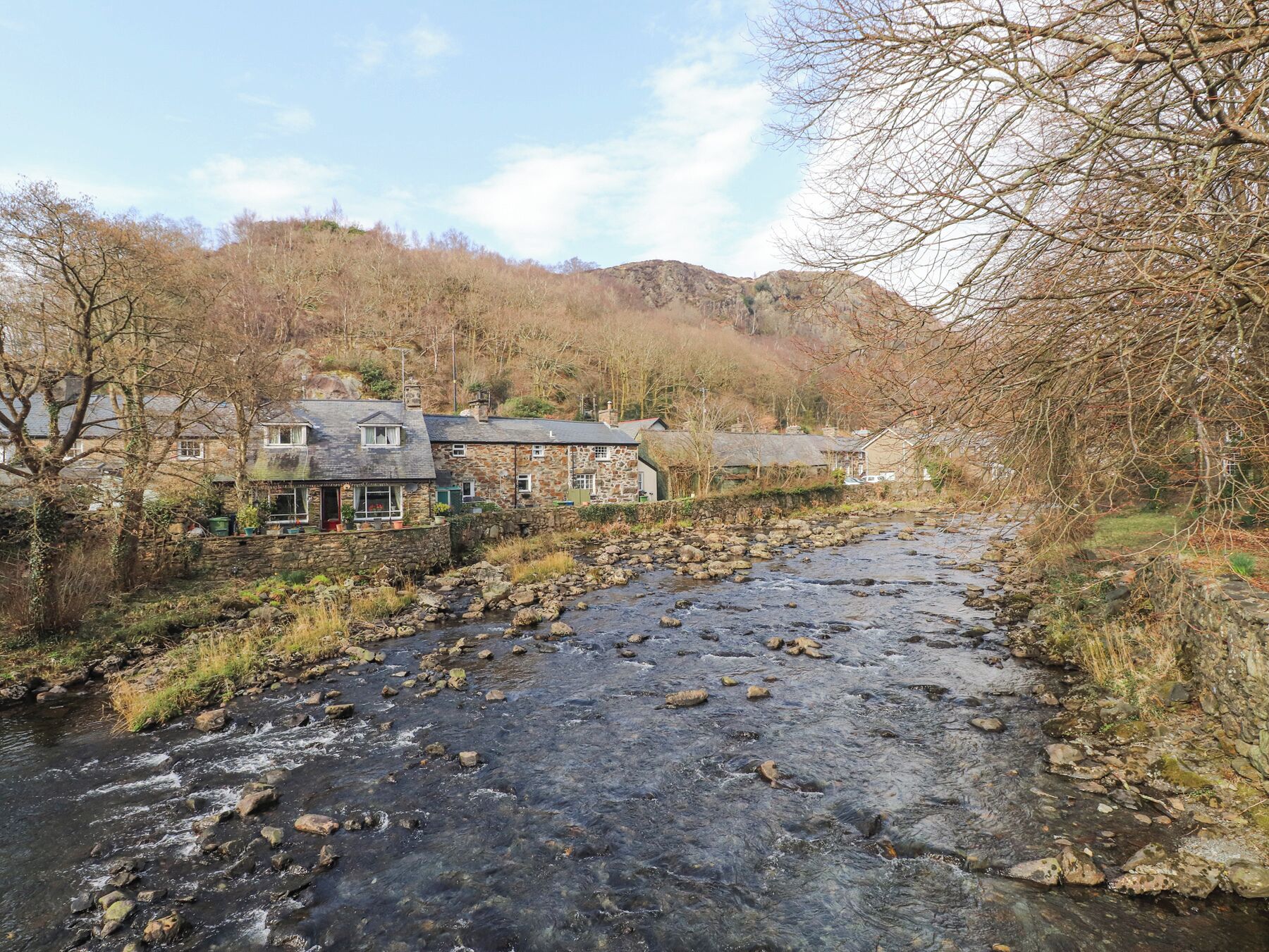 Un edificio de piedra con un letrero de pub, un río con rocas y una colina al fondo.