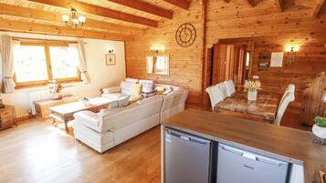 A cozy cabin-style room with a wooden interior, a sofa, a dining table, and a built-in refrigerator.