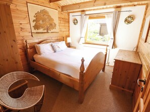 A wooden room with a bed, a wicker chair, a small wooden cabinet, and a window with curtains.