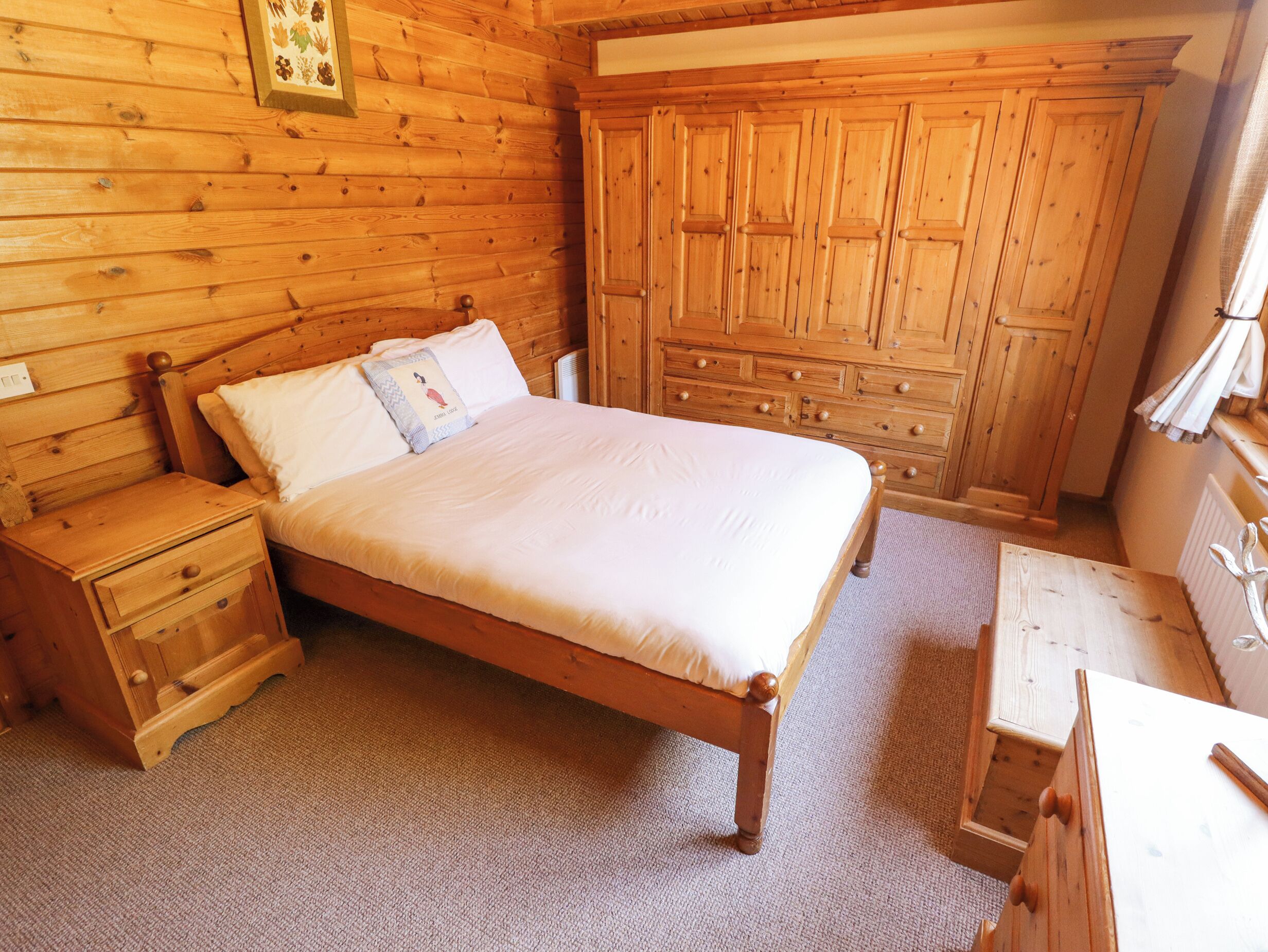 A wooden bedroom with a bed, nightstands, a dresser, and a small table.