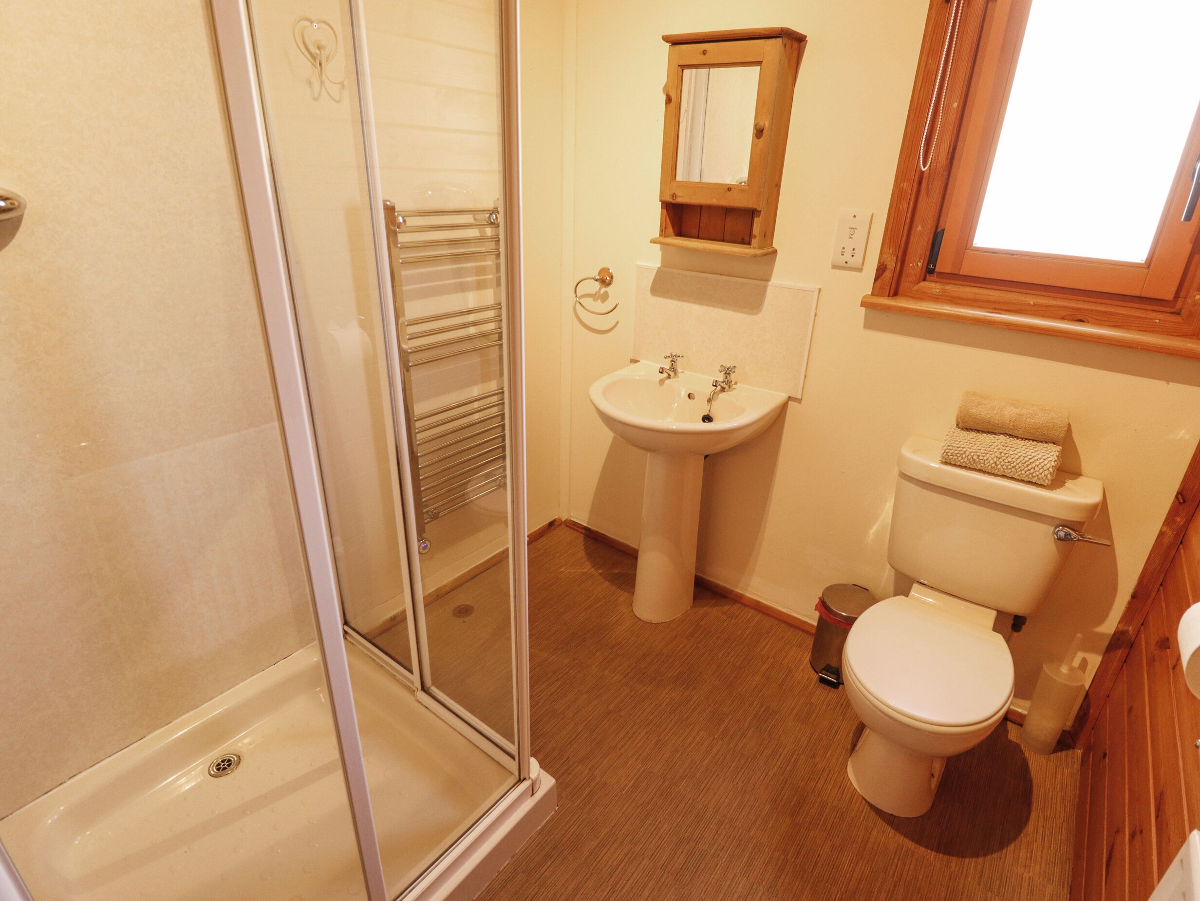Un baño con cabina de ducha de vidrio, lavabo pedestal y retrete.